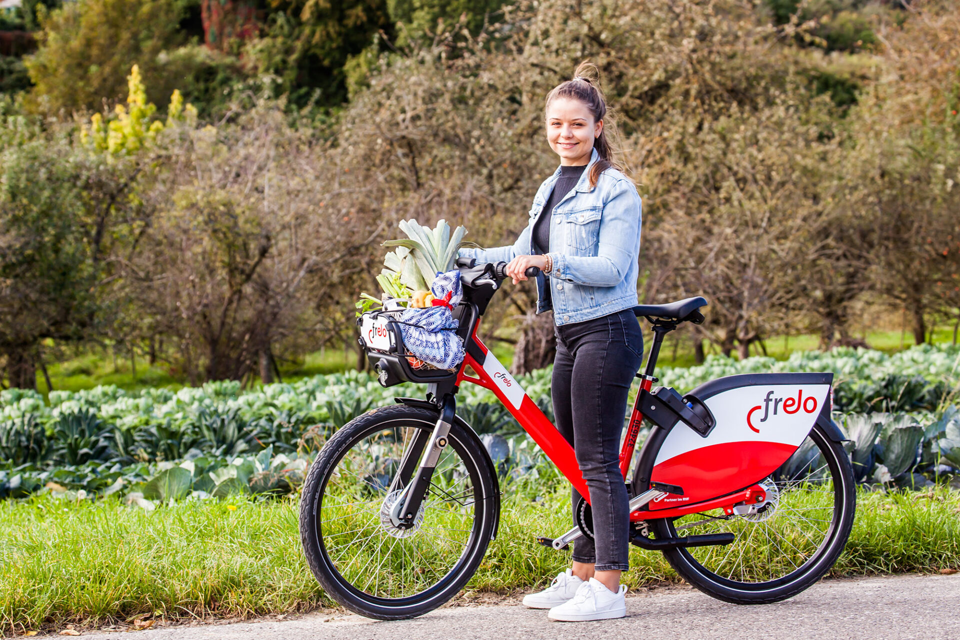 Junge Frau steht neben ihrem Frelo Leihrad, den Wochenmarkteinkauf im Korb.